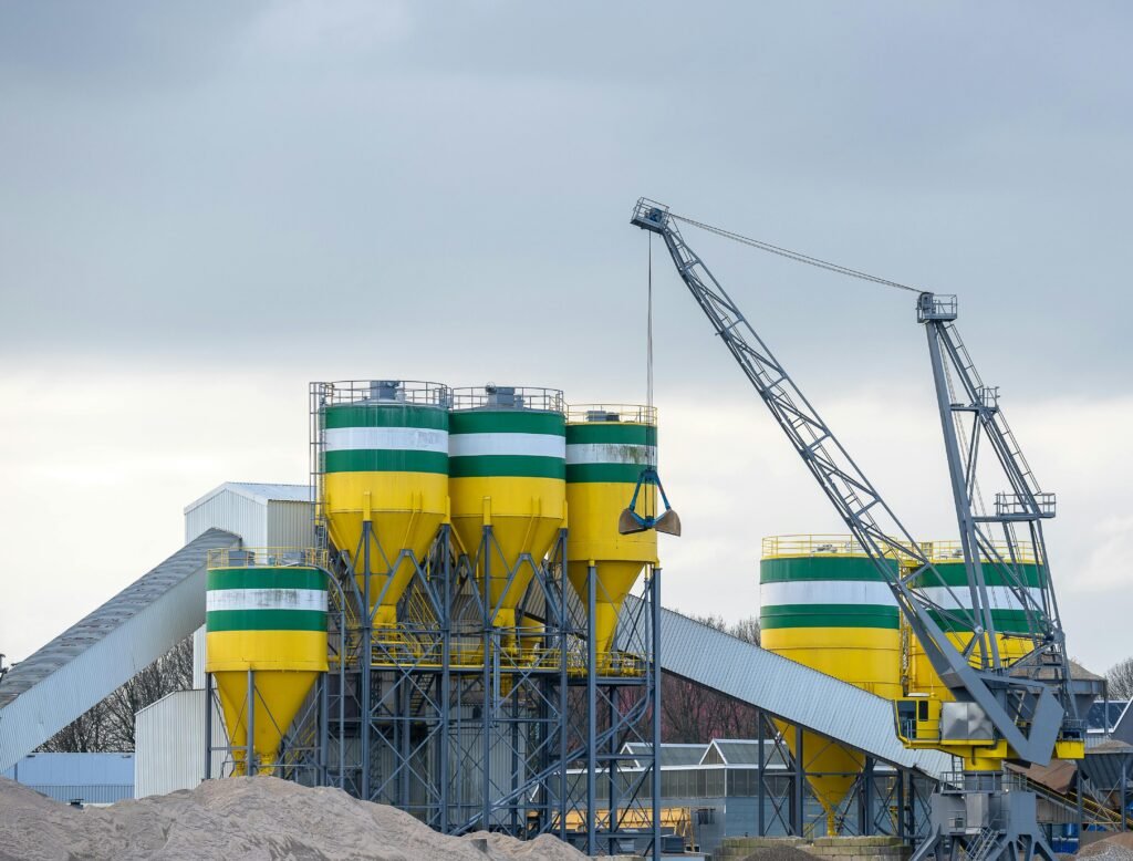 A large industrial crane working with silos at a modern cement plant under cloudy skies.