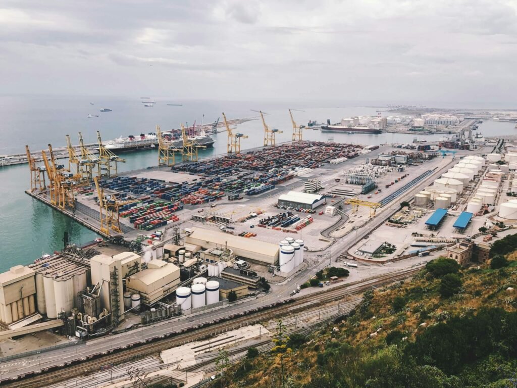 An aerial view of a busy industrial cargo port with cranes, containers, and ships.